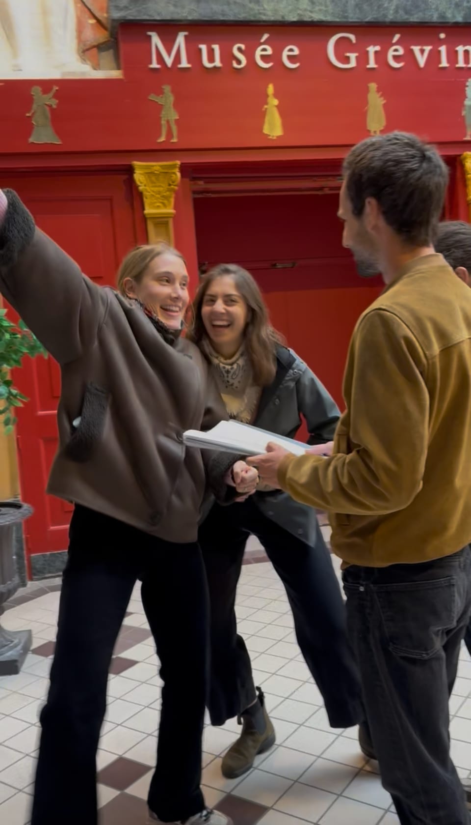 Deux joueuses rient aux éclats devant l'entrée du musée Grévin, un troisième joueur tient les Mémoires